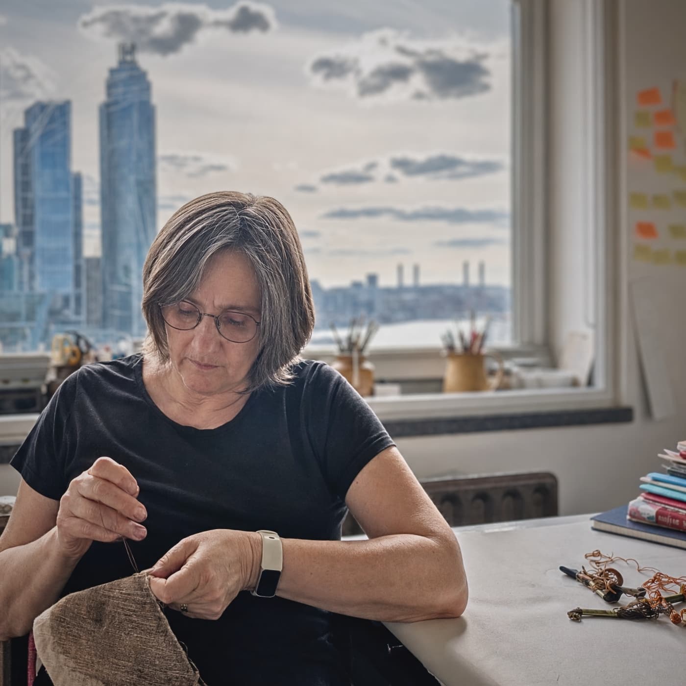 Textile artist Myra Stimson, sewing with city skyline backdrop.