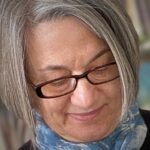 A close up image of textile artist Ana Buzzalino with glasses and blue scarf.