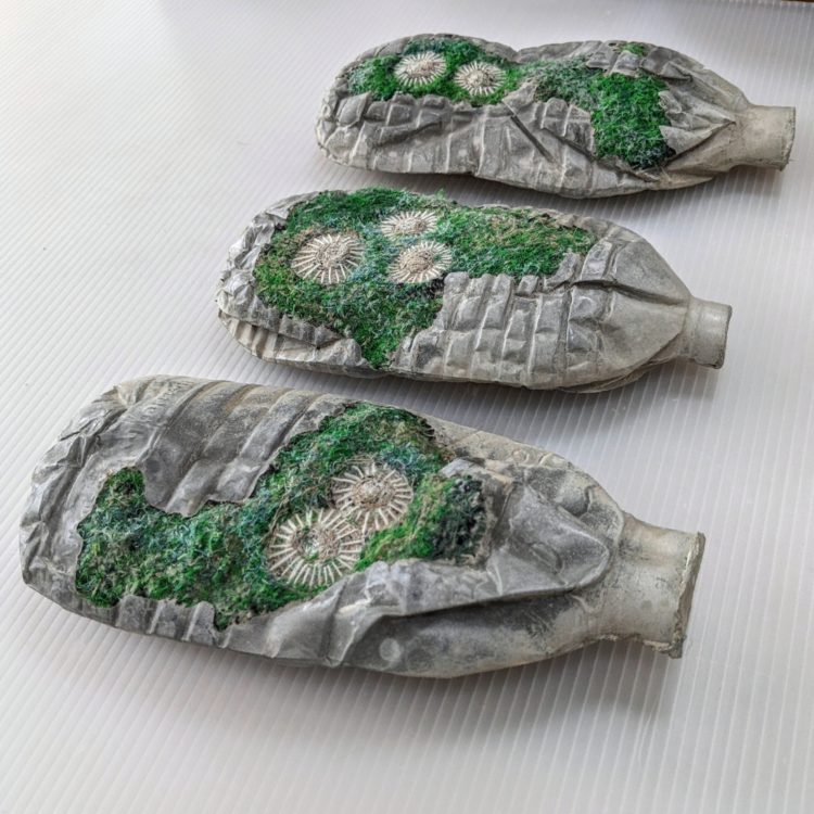 Nerissa Cargill Thompson, Message in a Bottle: Three Green Bottles, 2021. Each bottle: 20cm x 9cm x 3.5cm (8" x 3½" x 1½"). Embellished and embroidered recycled textiles, concrete, plastic waste trays. Embellishing, hand and machine embroidery, casting.