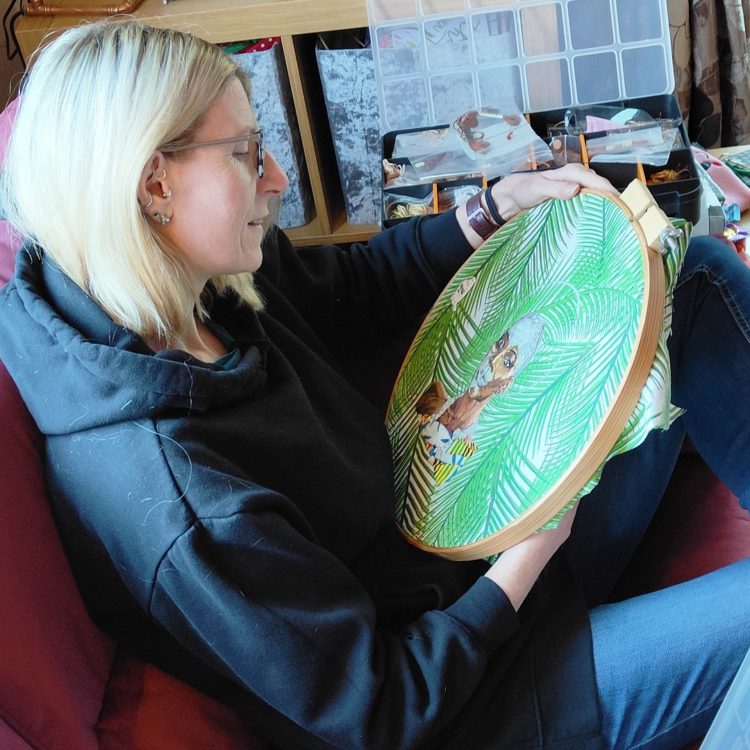 Jane C Thom working on an embroidery on her sofa