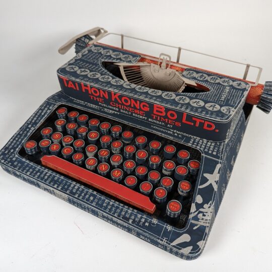Jennifer Collier, Canada’s 1923 Chinese Exclusion Act Paper Typewriter, 2022. 32cm x 32cm x 9cm (12½" x 12½" x 3½"). Machine stitch and paper manipulation. Made from papers designed by the commissioner using vintage newspapers. Paper, grey board and machine stitch.
