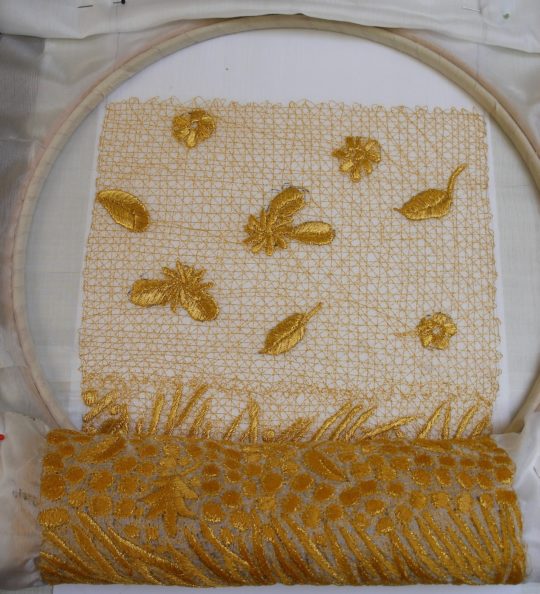 Kate Wells: Leaves and flowers stitched onto an embroidered grid on dissolvable fabric, showing the roll of stitched cloth below.Kate Wells: Leaves and flowers stitched onto an embroidered grid on dissolvable fabric, showing the roll of stitched cloth below.