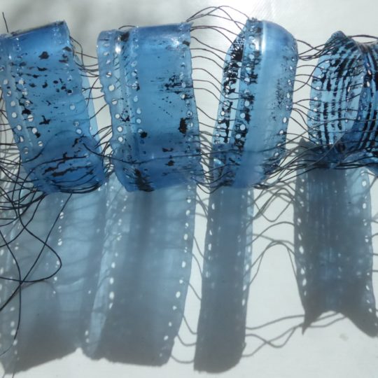 Siân Martin, Blue Bottle, 2019. 20cm x 5cm (8" x 2"). Discarded plastic bottle, linen threads. Melted plastic with perforated holes and mending stitches.