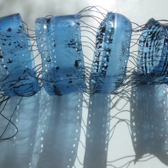 Siân Martin, Blue Bottle, 2019. 20cm x 5cm (8" x 2"). Discarded plastic bottle, linen threads. Melted plastic with perforated holes and mending stitches.