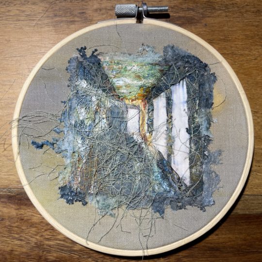 Ruth Norbury, Compliance, 2022. Hoop 14cm (5.5”) diameter. Cotton fabric, stranded cotton, paint, ink, scrim, Lutradur, spray paint. Hand embroidery, appliqué, stenciling, painting, inking.