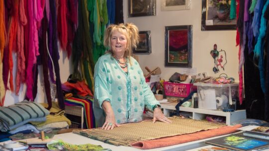 Moy Mackay in her studio surrounded by colourful materials.