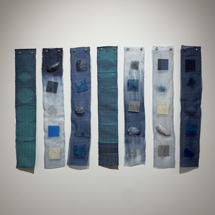 Amanda Britton, One Blue from Another, 2023. Seven strips, each 10cm x 51cm (4" x 20"). Weaving, dyeing, resin casting, machine stitching. Organza, indigo dye, Johanna Norry’s woven remnants, grommets, resin, shells, polyester thread.