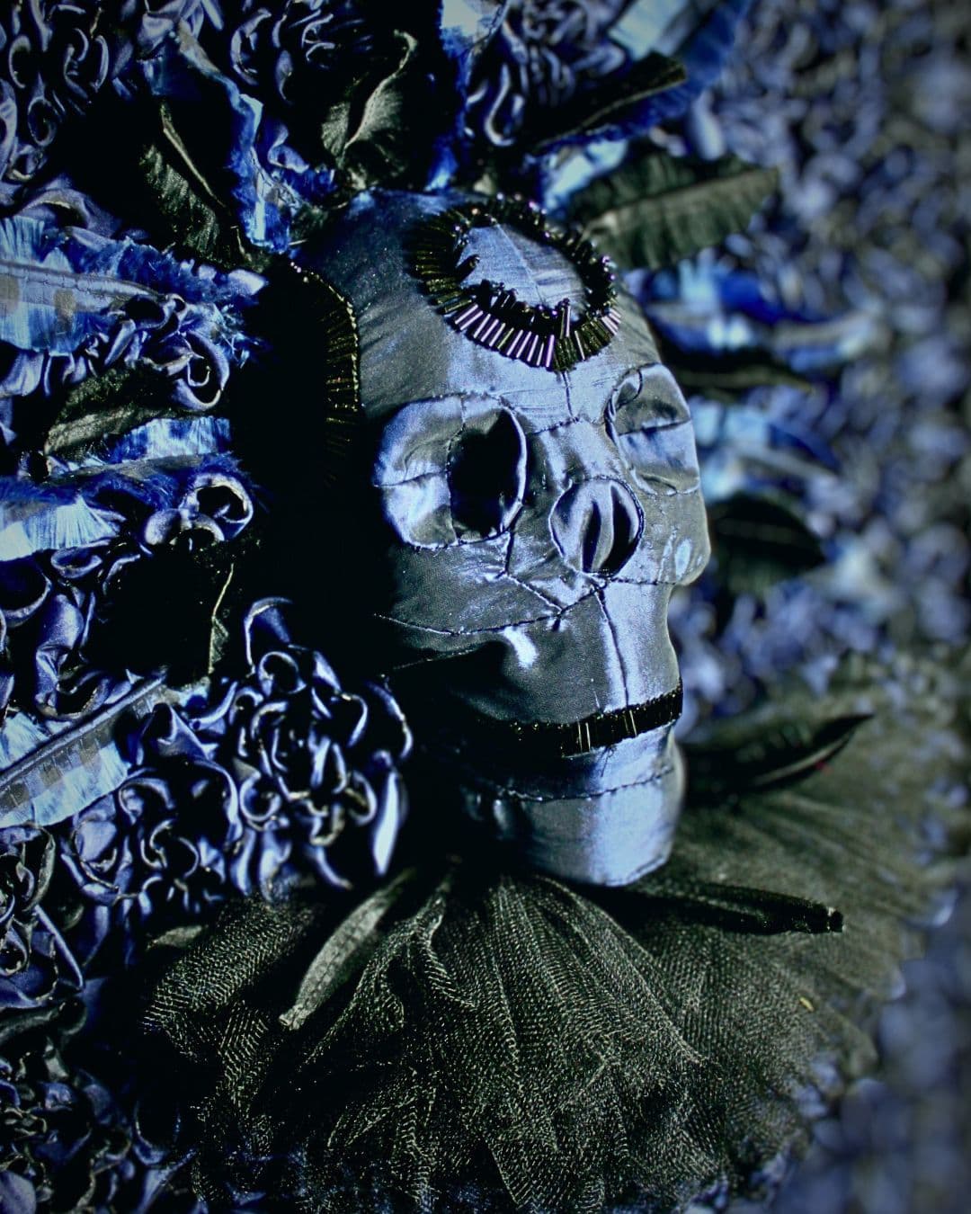 A close up of a decorative skull made with blue embellishments in various textile materials.