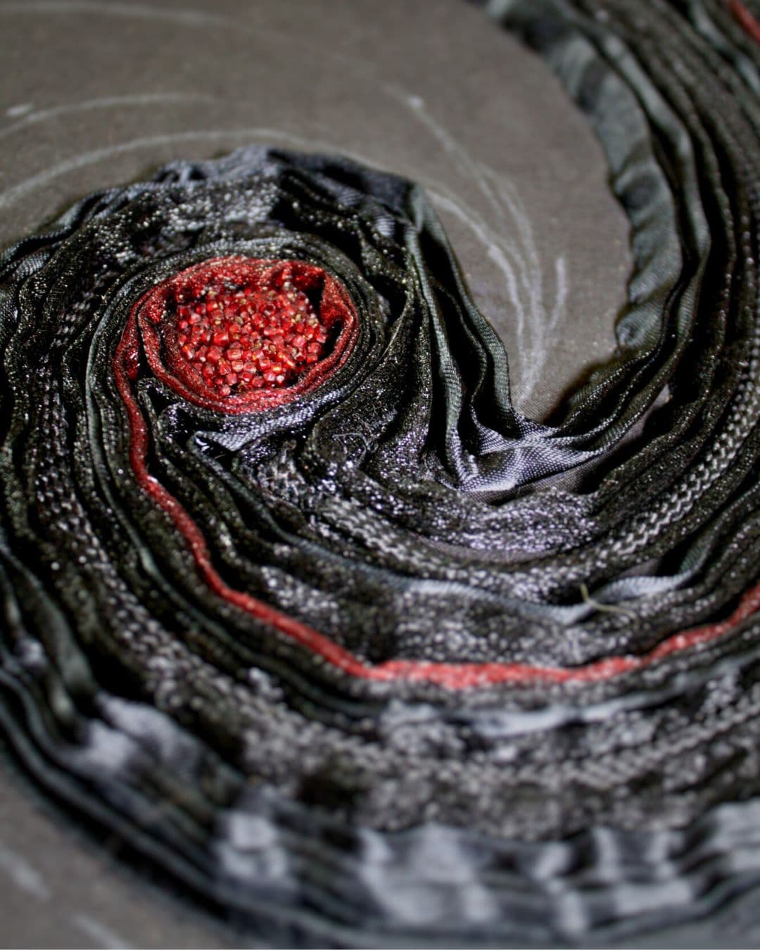 Textured artwork of a circular black and red swirling pattern.