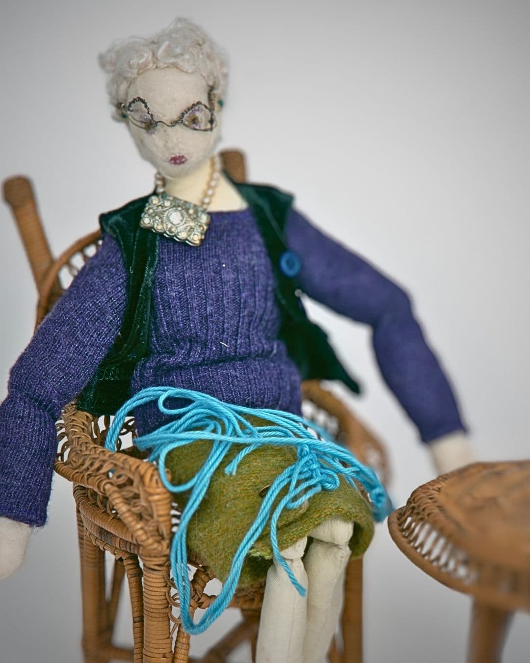 a handstitched woolen doll sitting in a chair with embroidery work