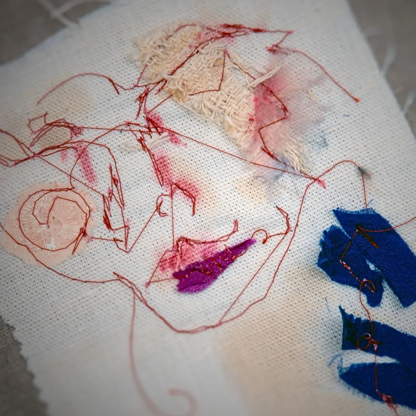 A hand embroidery & ink collage of a face using linen on canvas