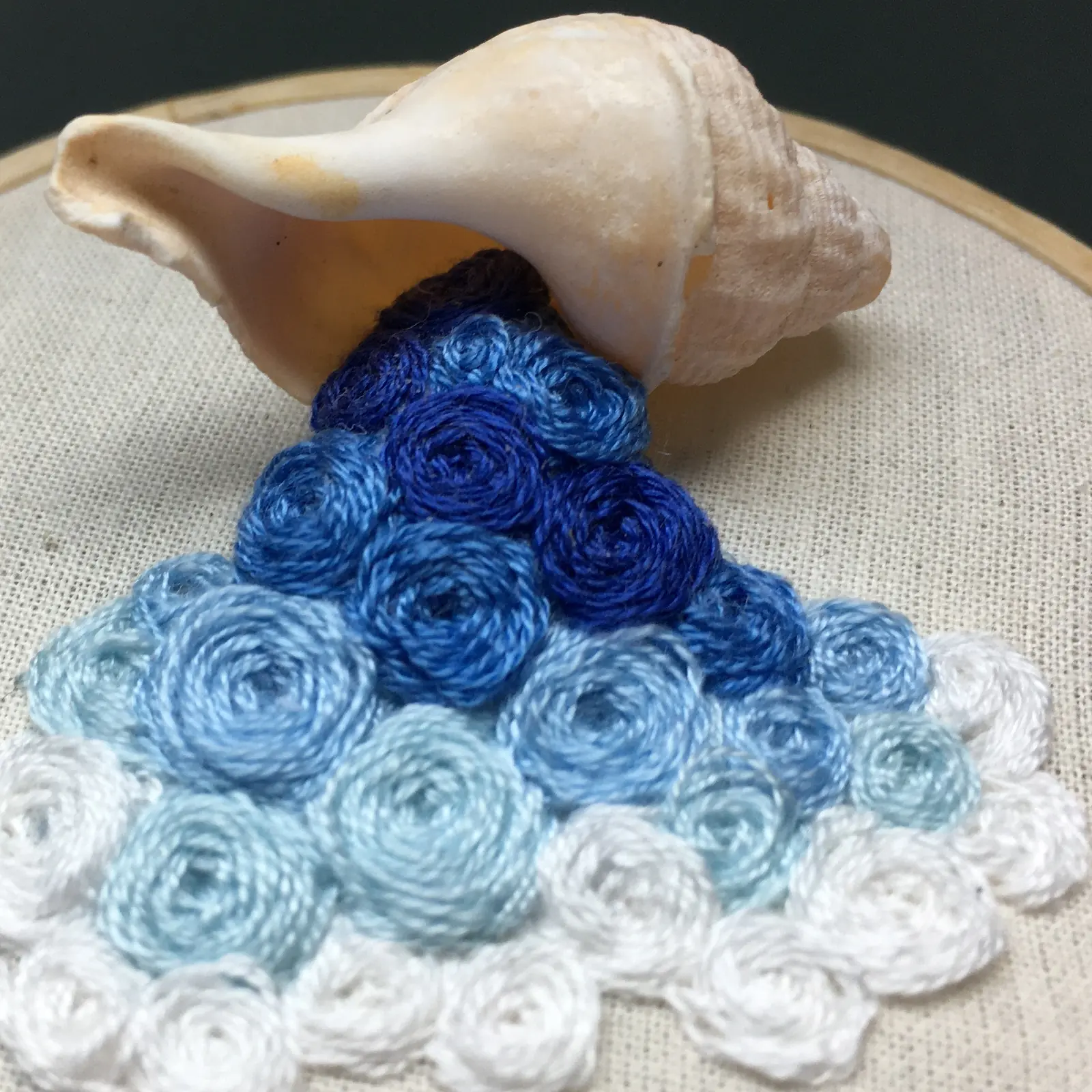 A seashell and blue and white threads on an embroidery hoop