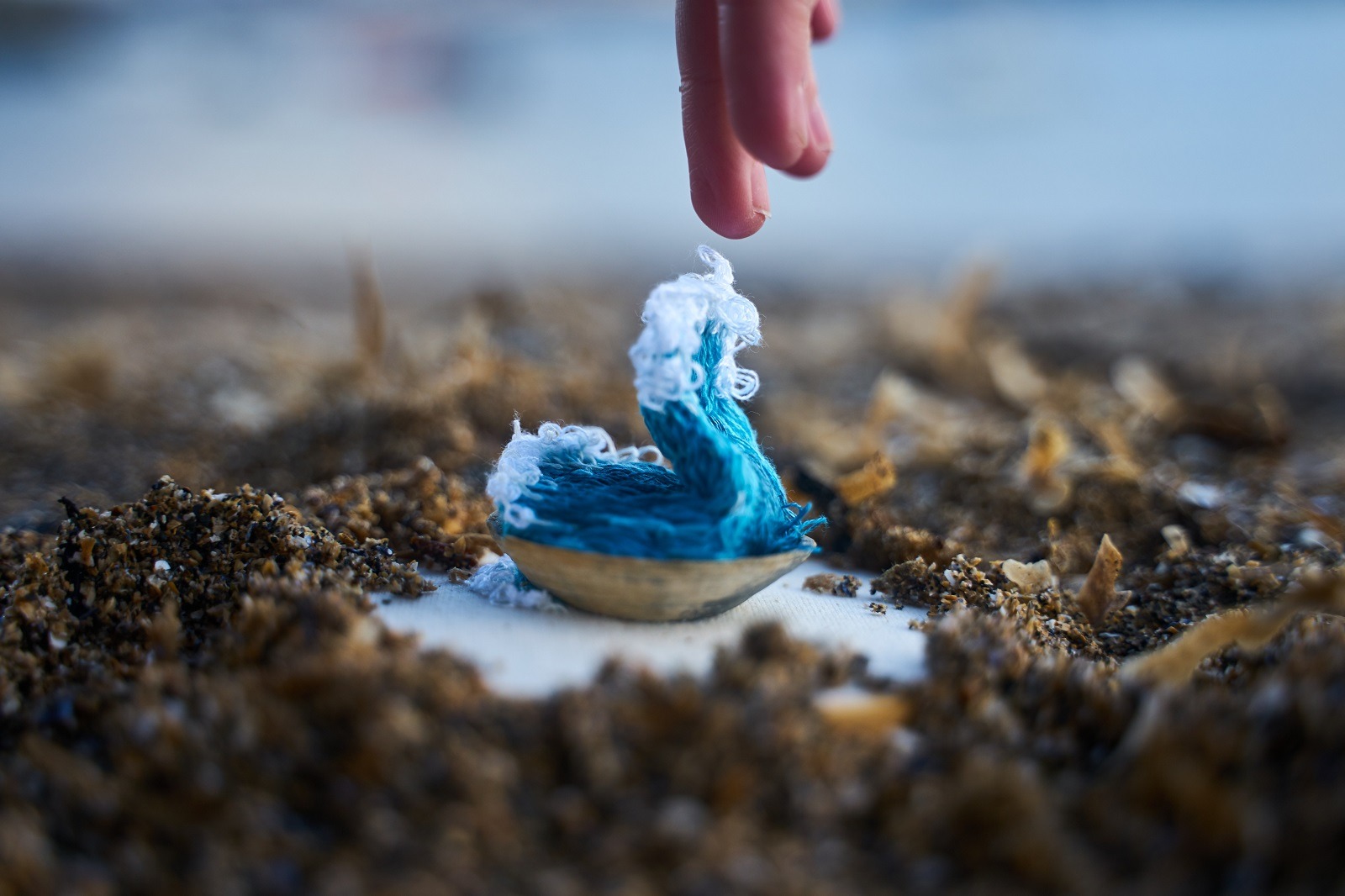 A finger touching a blue thread wave coming out of a shell