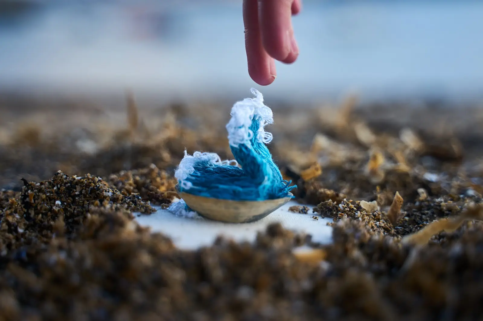 A finger touching a blue thread wave coming out of a shell