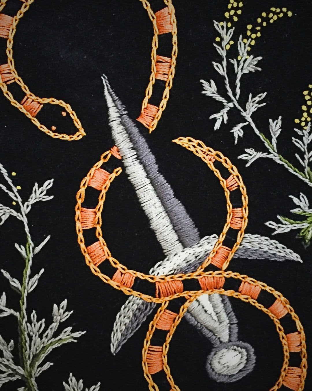 A close up of a fabric with embroidery of dagger and snake