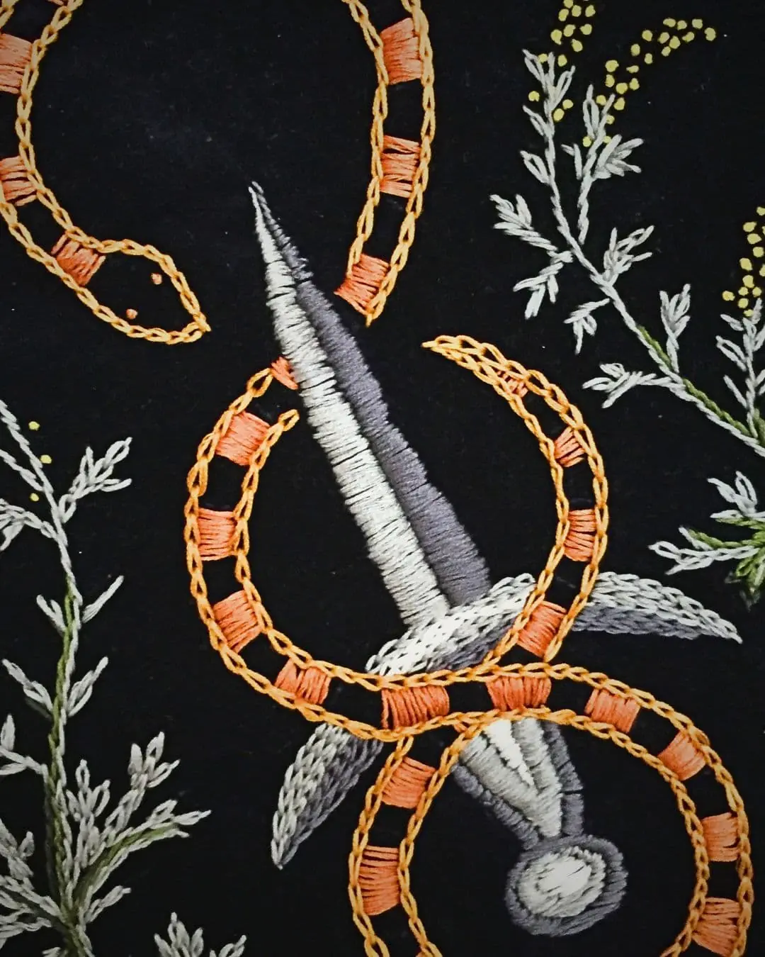 A close up of a fabric with embroidery of dagger and snake