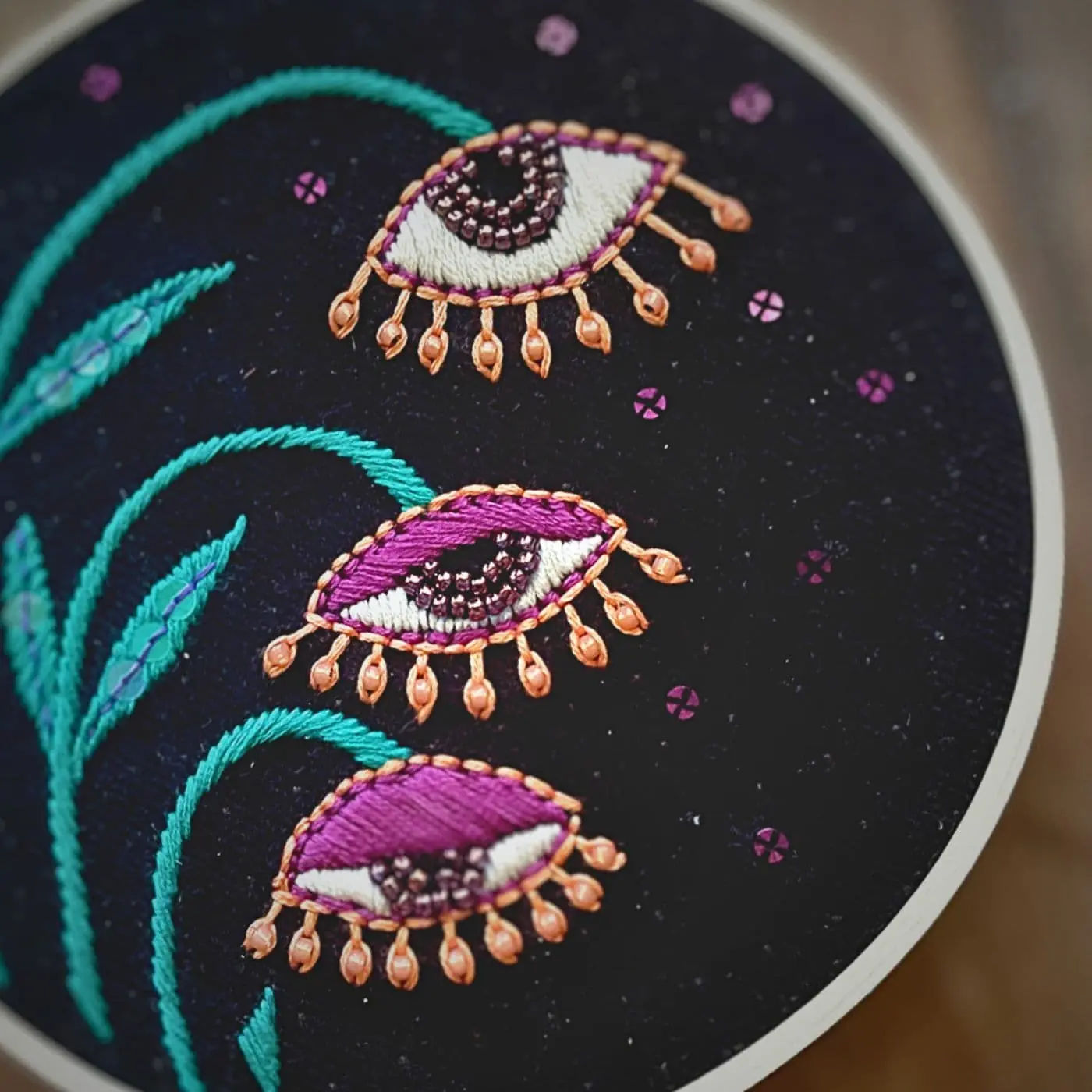 A close up an embroidery hoop with stylized eyes on plants