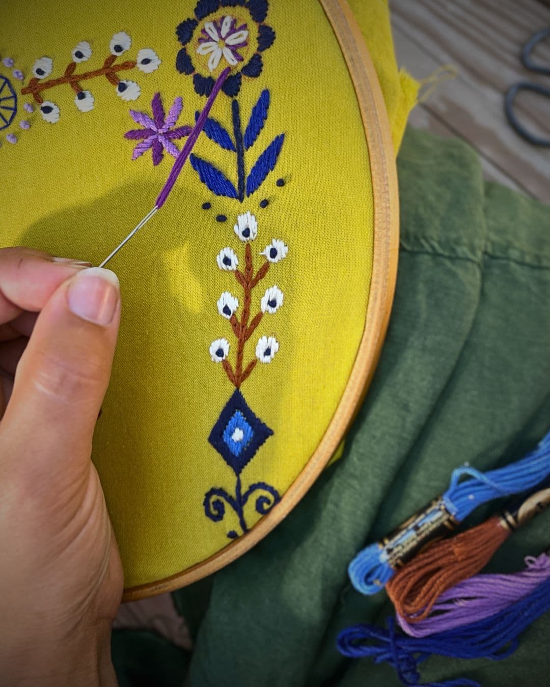Hand holding a needle with a colorful embroidery design on a yellow fabric