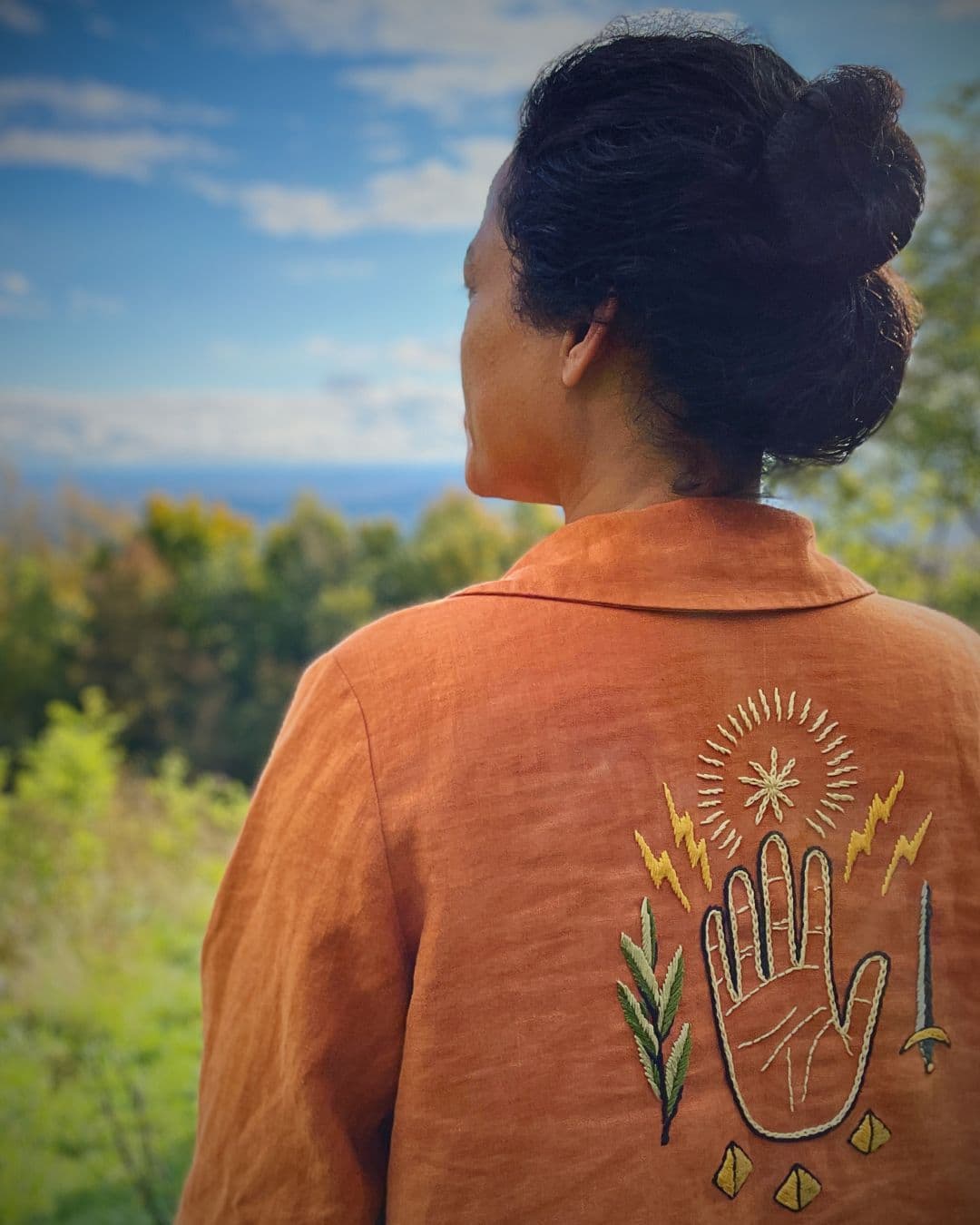 Textile Artist Christi Johnson in orange jacket with a hand embroidered on the back