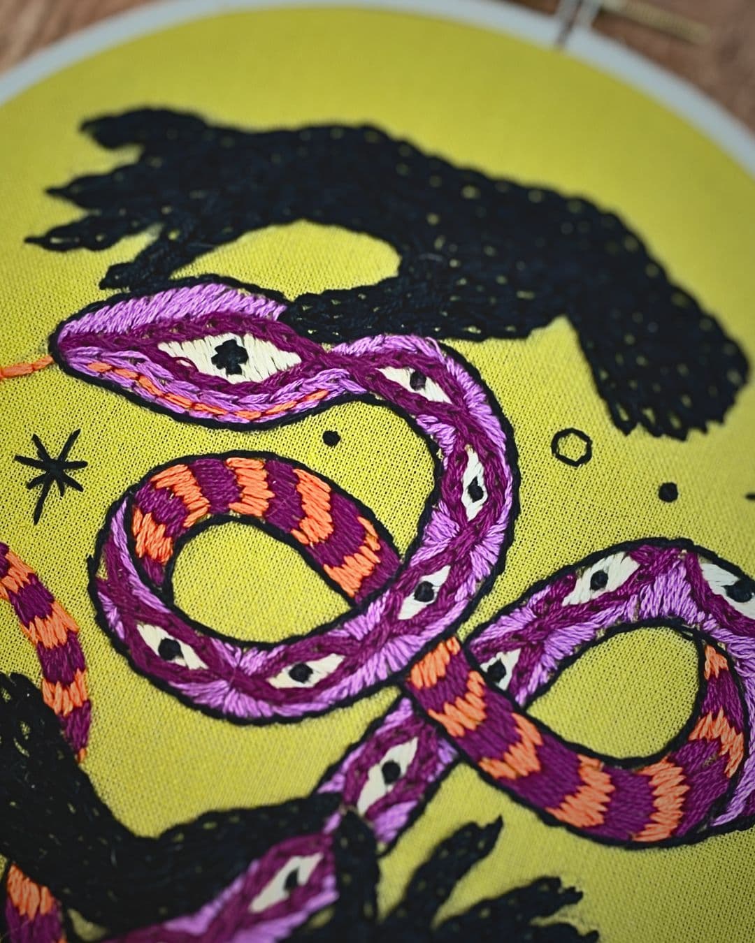 Embroidery hoop with stitched hands and a purple serpent
