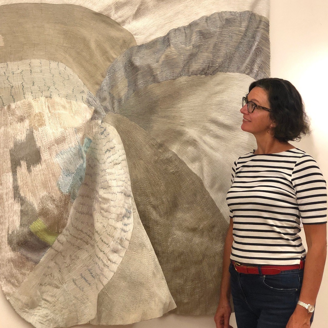 Textile Artist Dionne Swift stood beside one of her textile art pieces hanging