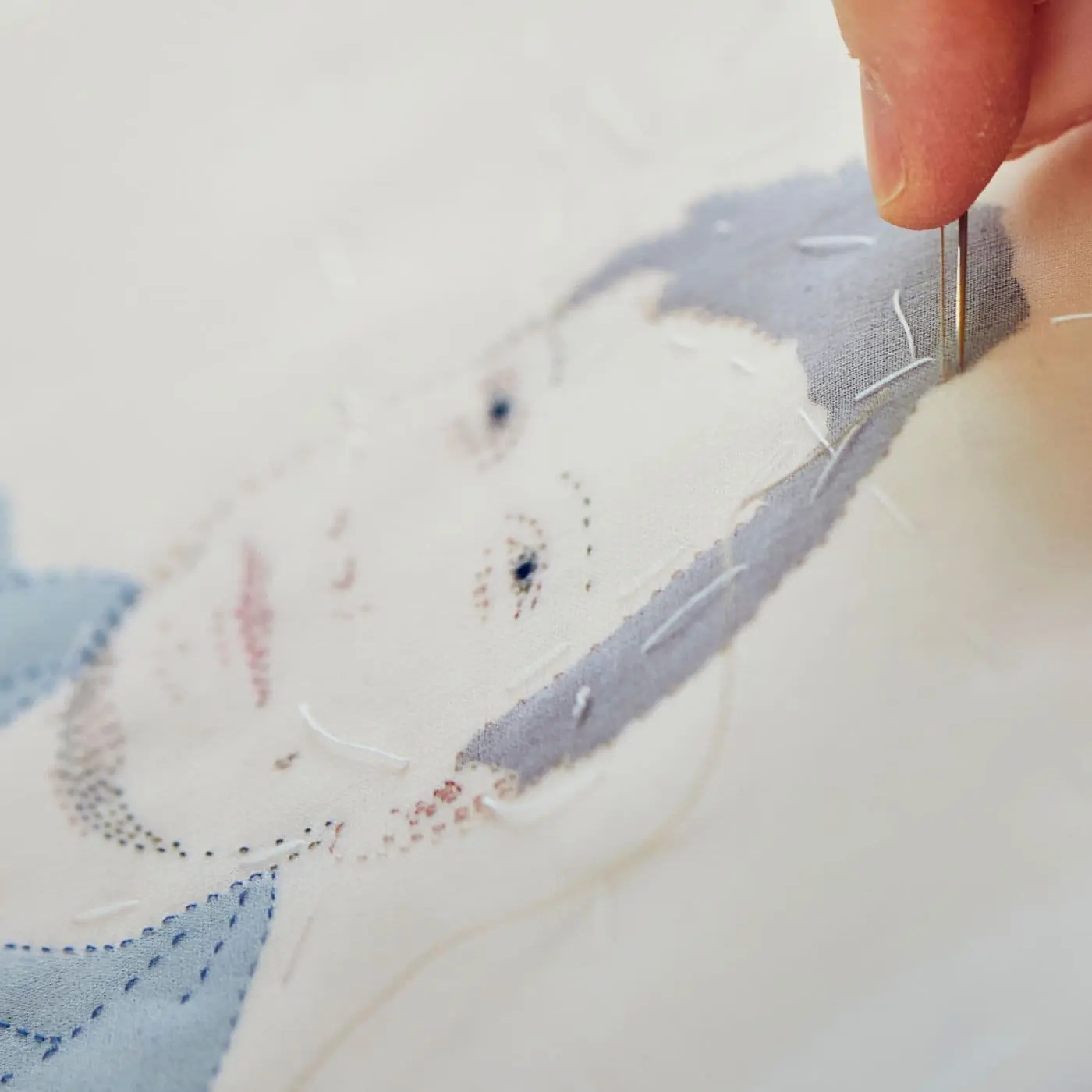 Close up of an artist at work on a stitched textile artwork of a boy's face.