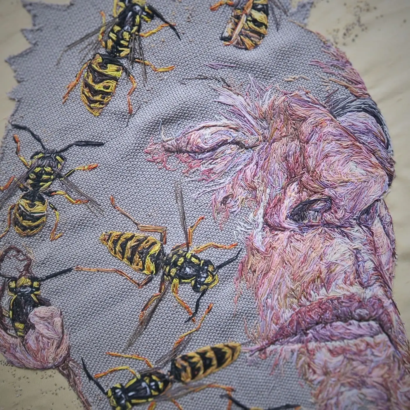 A thread painting of a man's face covered in bees.