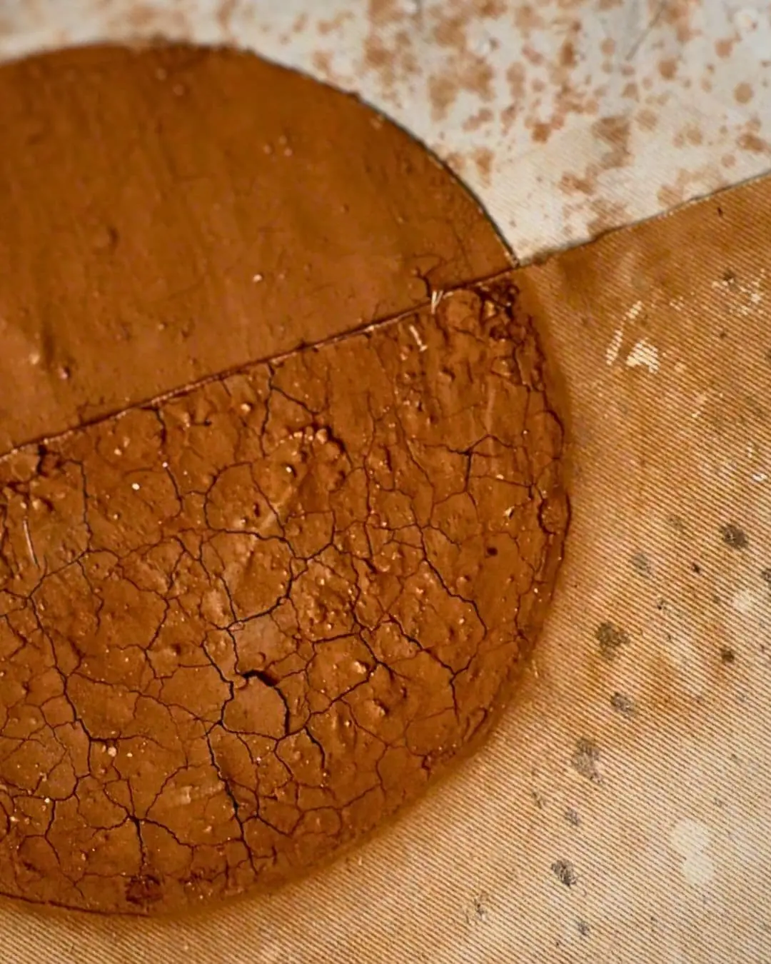 A close up of a textile artwork with a brown circle made out of mud