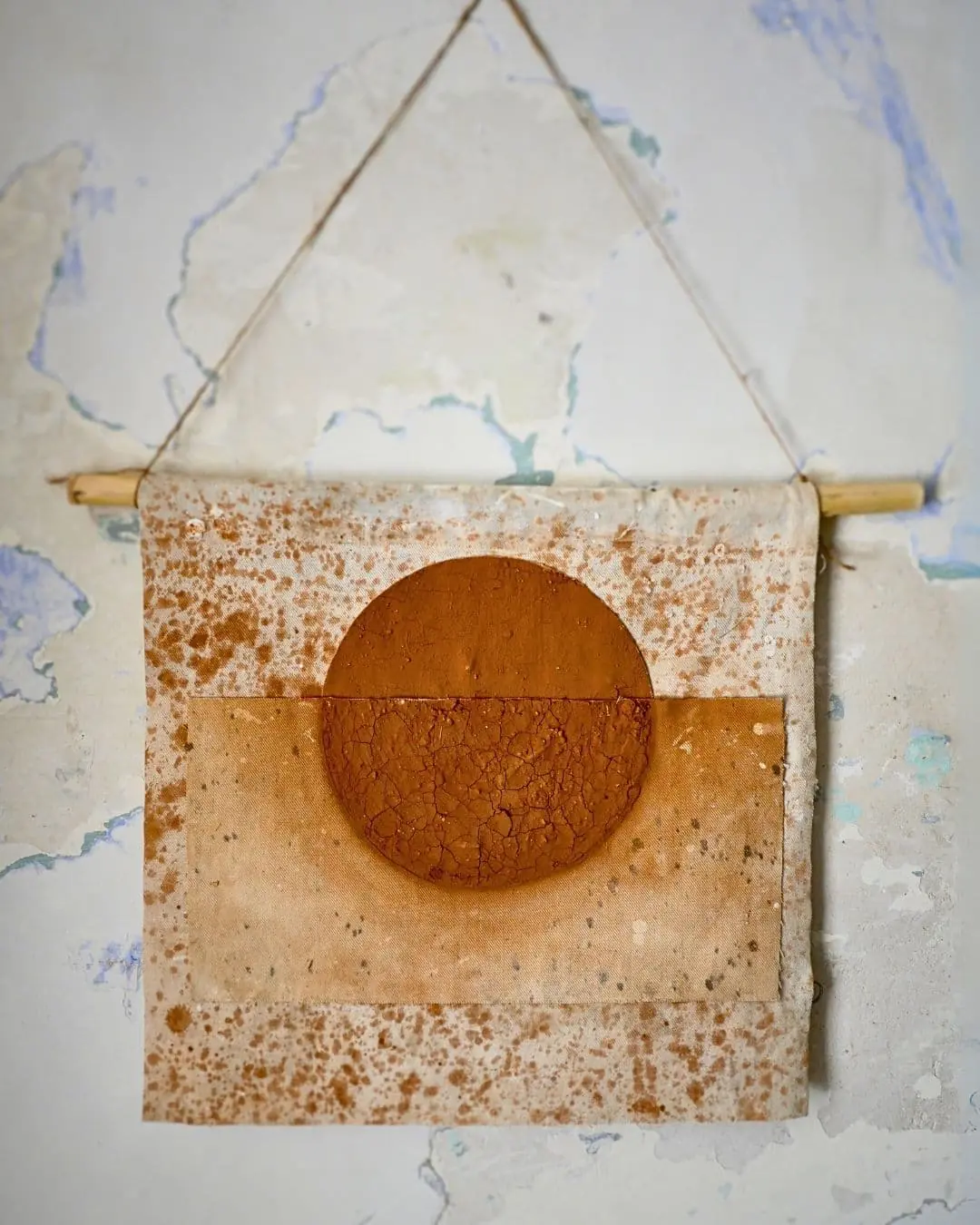 A textile art piece hanging from string with a clay circle on it
