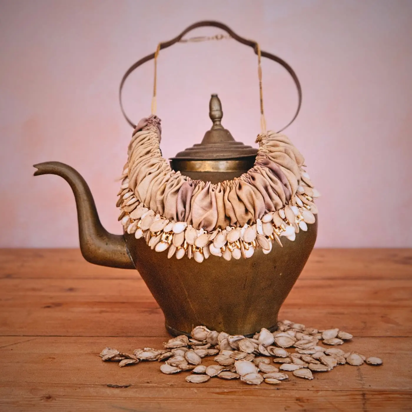 A vintage teapot with a necklace on top of it