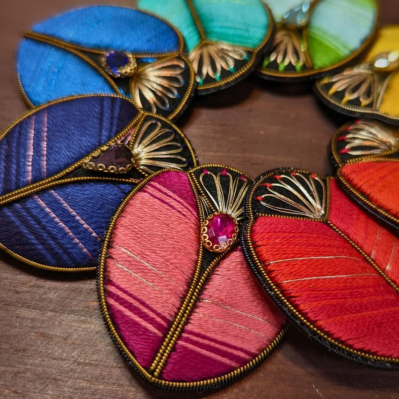 A group of colourful, hand stitched Beetle Brooches arranged in a circle. 