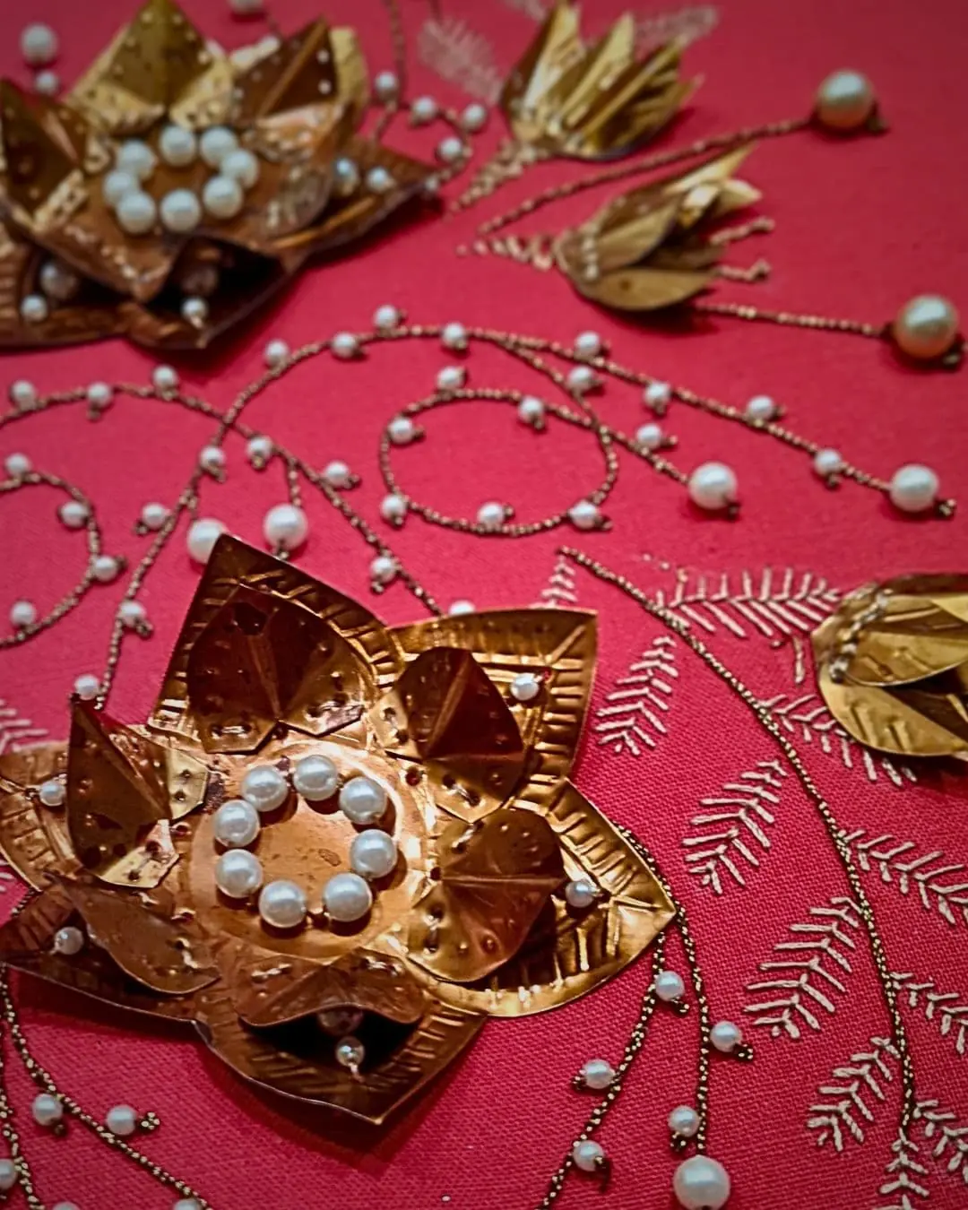 A close up of a metal flower art work embellished with beads on a red background. 