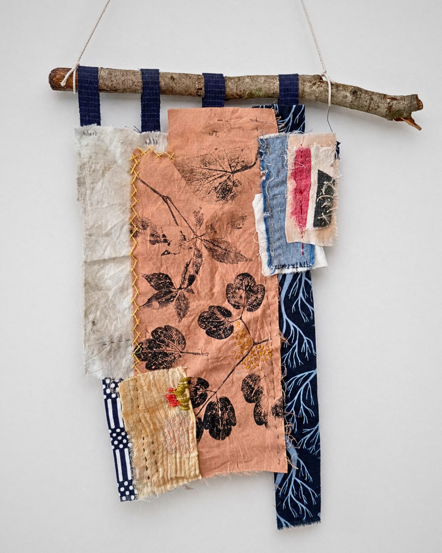 Textile art with natural motifs displayed hanging on a stick.