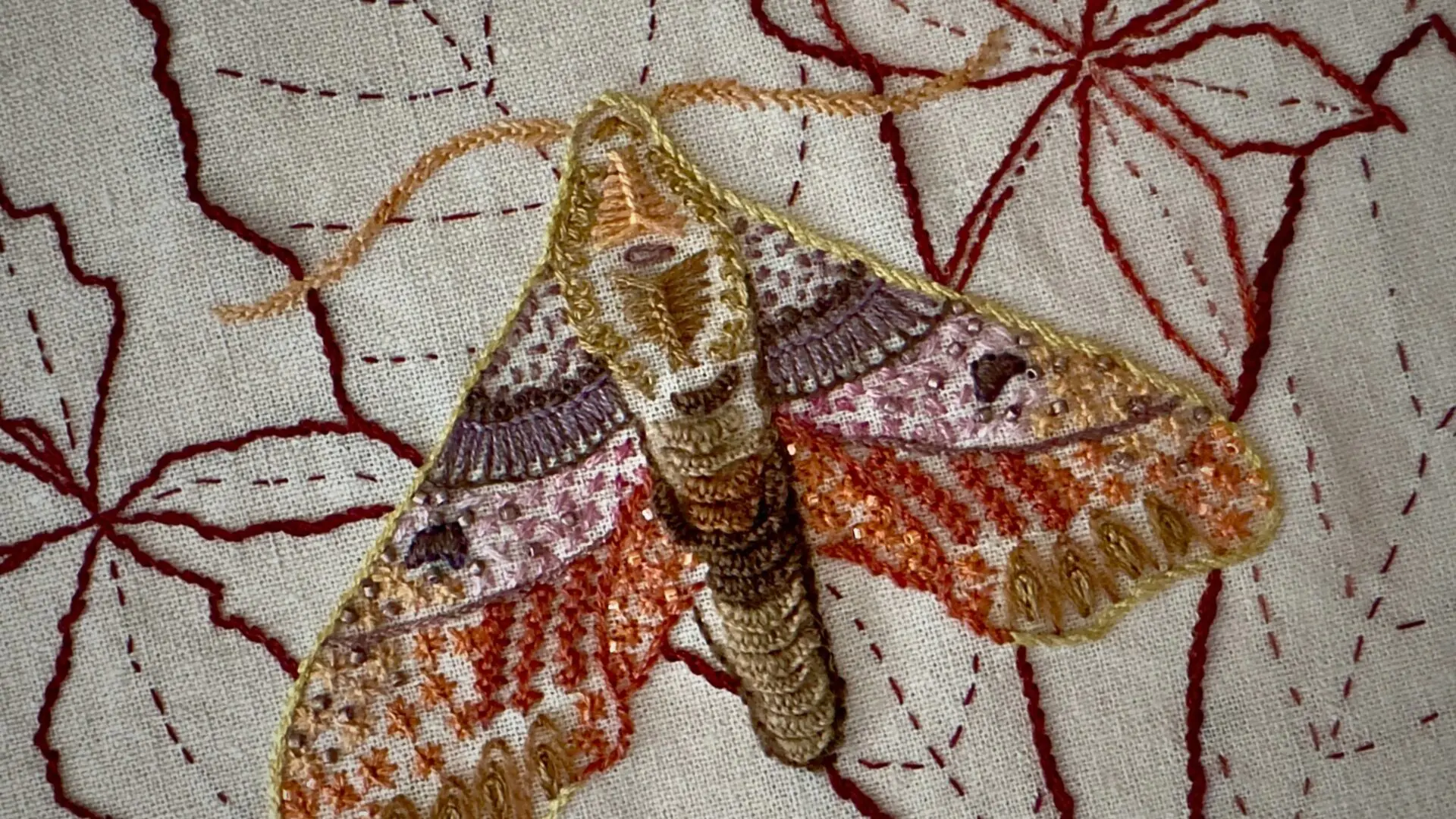 Embroidered moth on floral background.