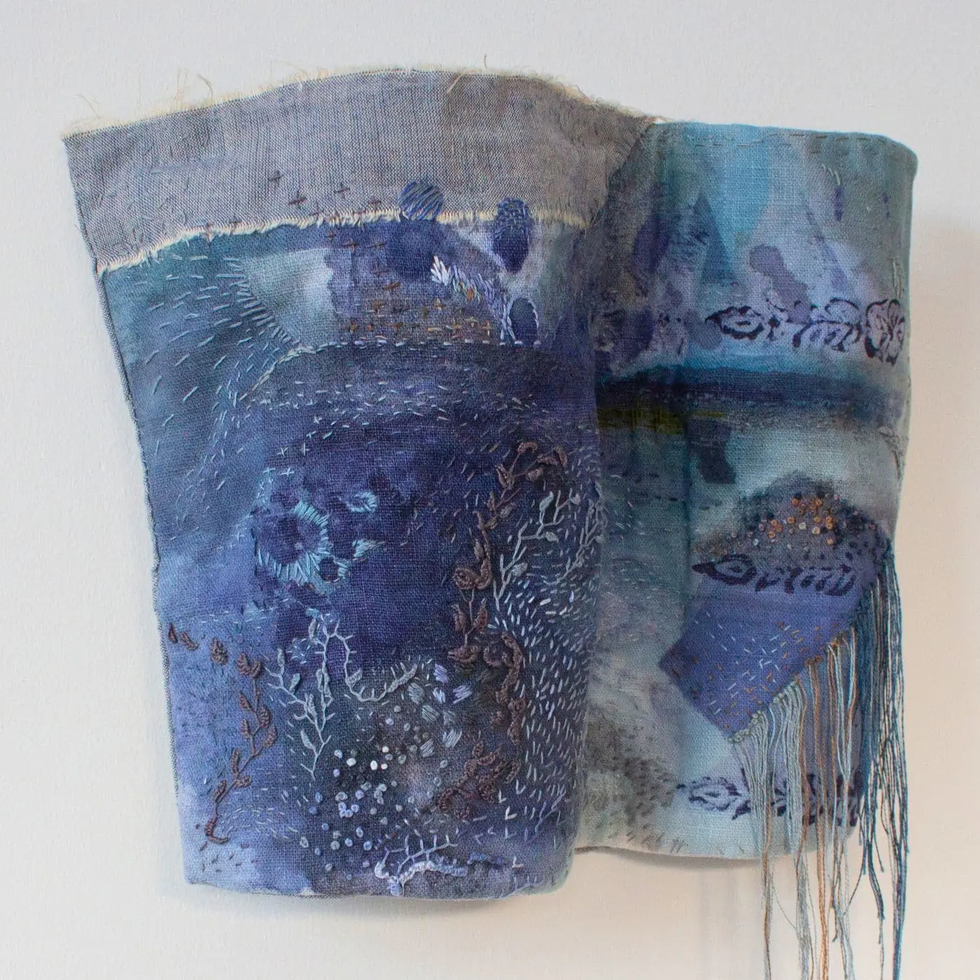 A stitched sculpture in the shape of a wave with a mix of blue colours and details and loose threads.
