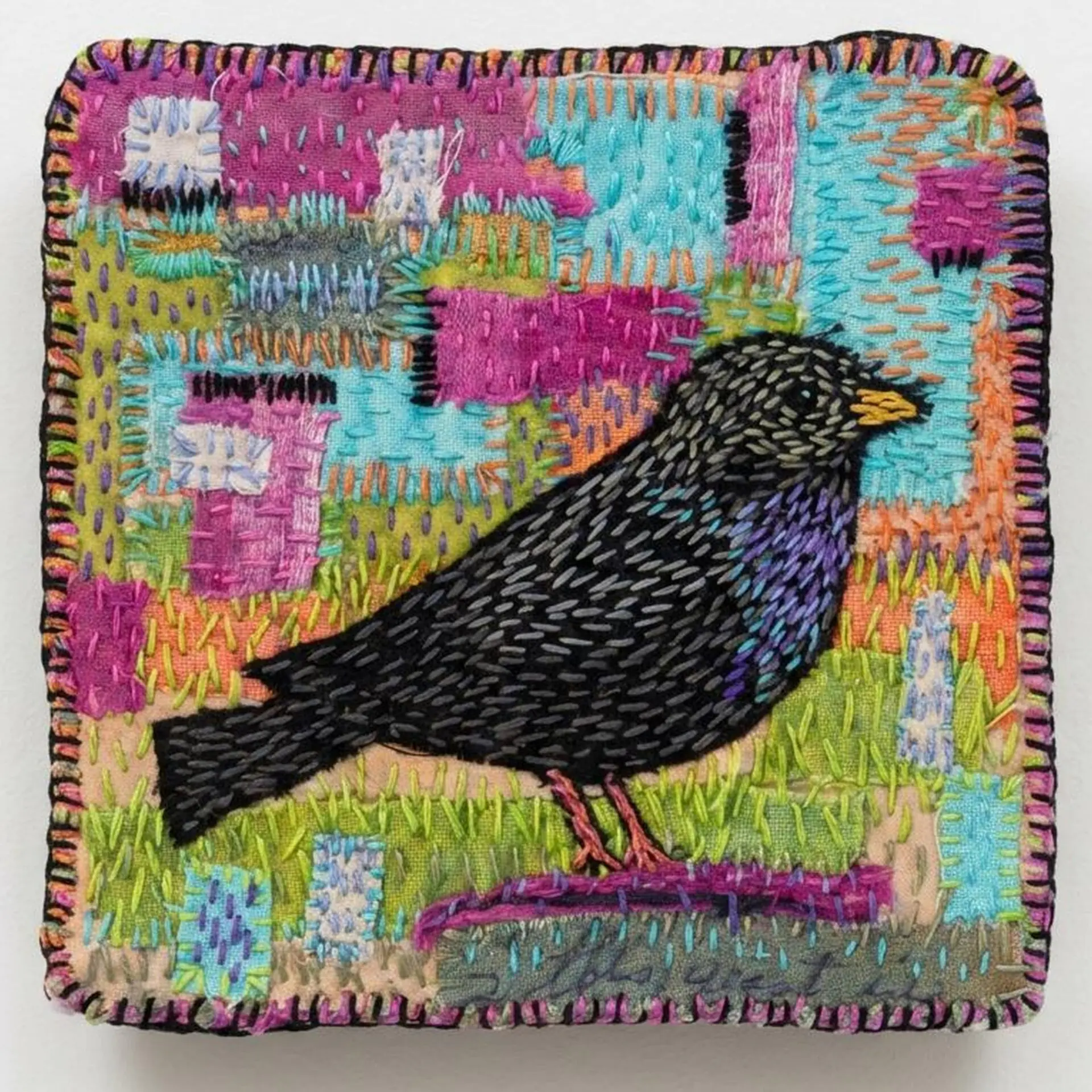 Colourful embroidered bird on stitched fabric