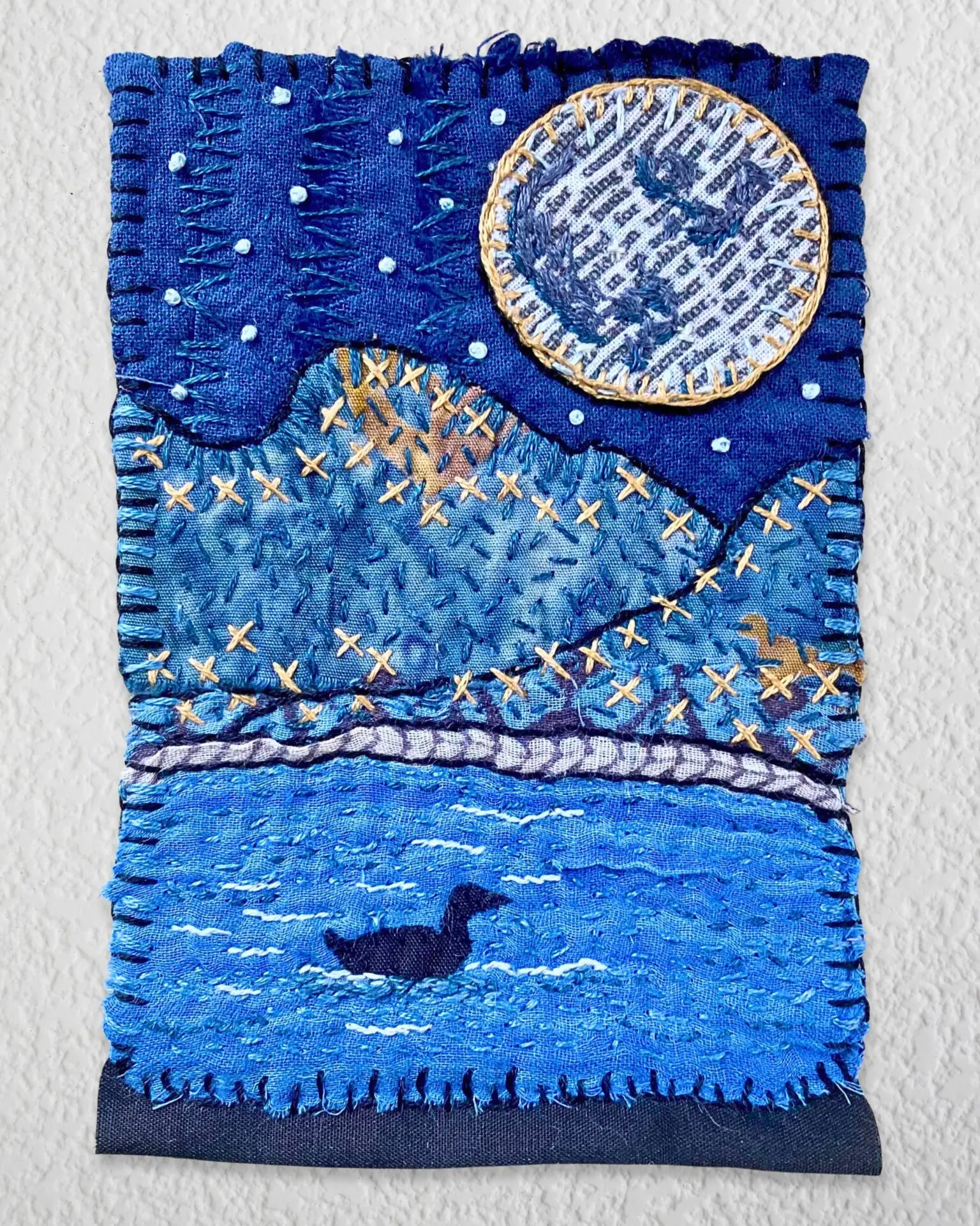 Textile art depicting moonlit landscape.