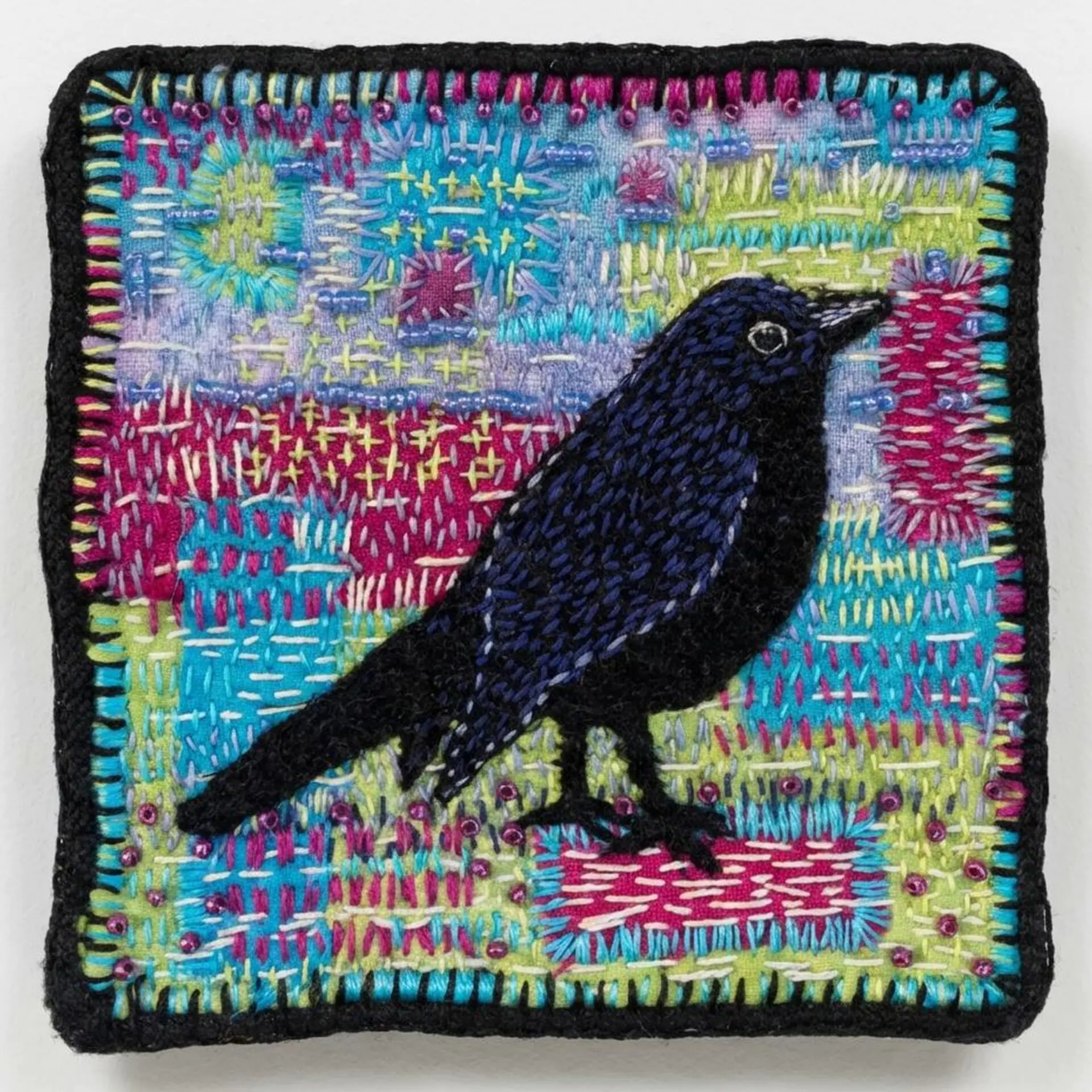 Embroidered black bird on colourful background.