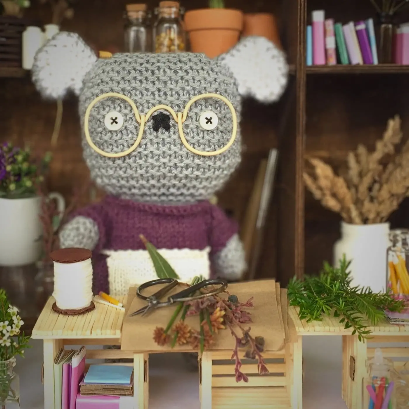 A knitted koala in a florist shop, surrounded by flowers.