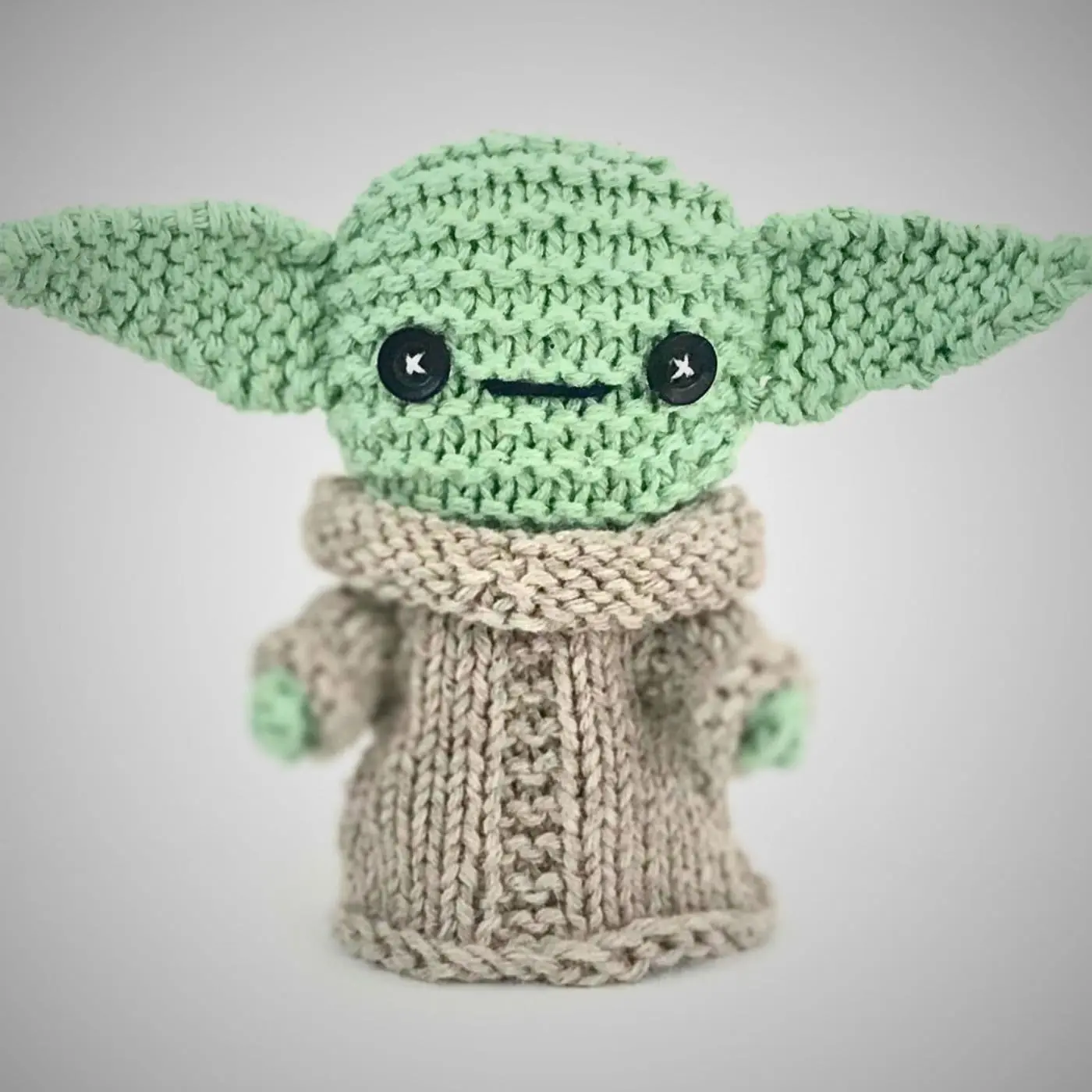 A knitted toy with green eyes and long ears resembling the character 'Yoda'. 