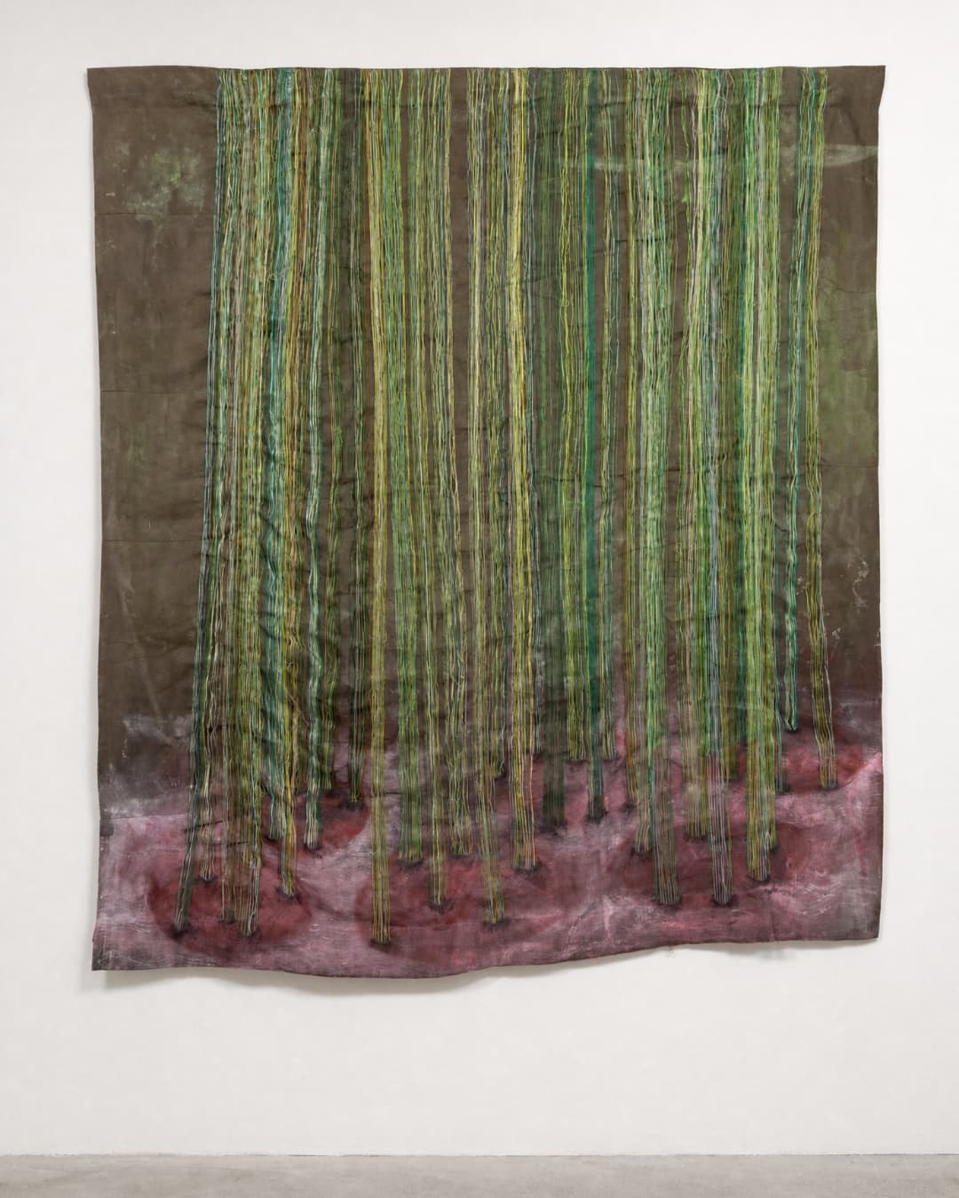 Textile artwork with vertical green strands hanging on wall in gallery