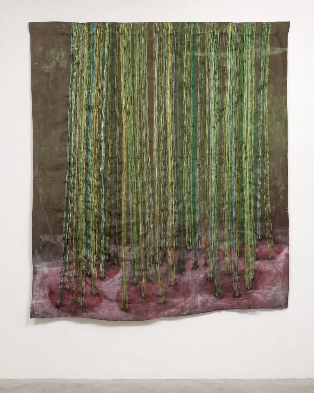 Textile artwork with vertical green strands hanging on wall in gallery