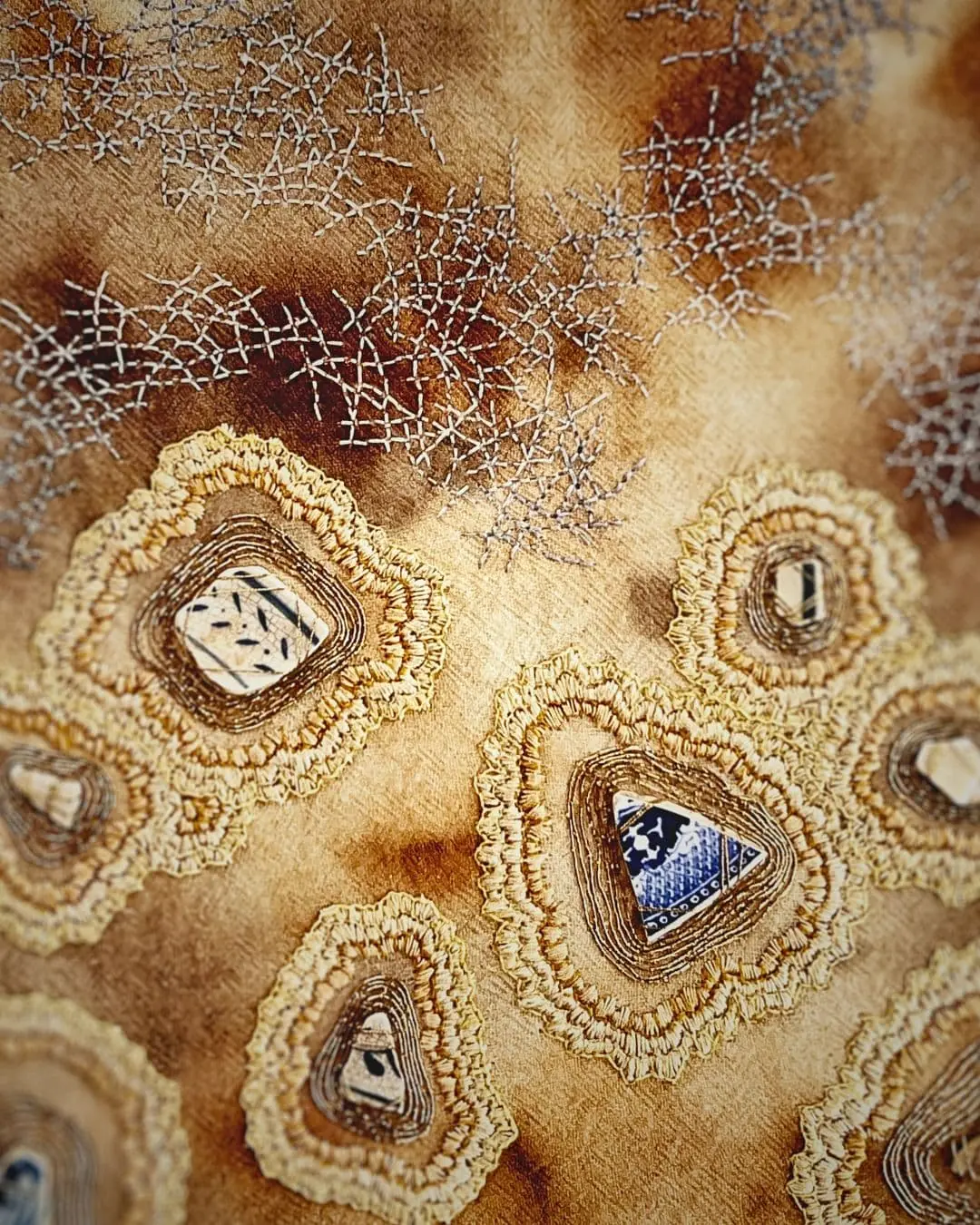A piece of textile art with fragments of pottery and embroidery around them