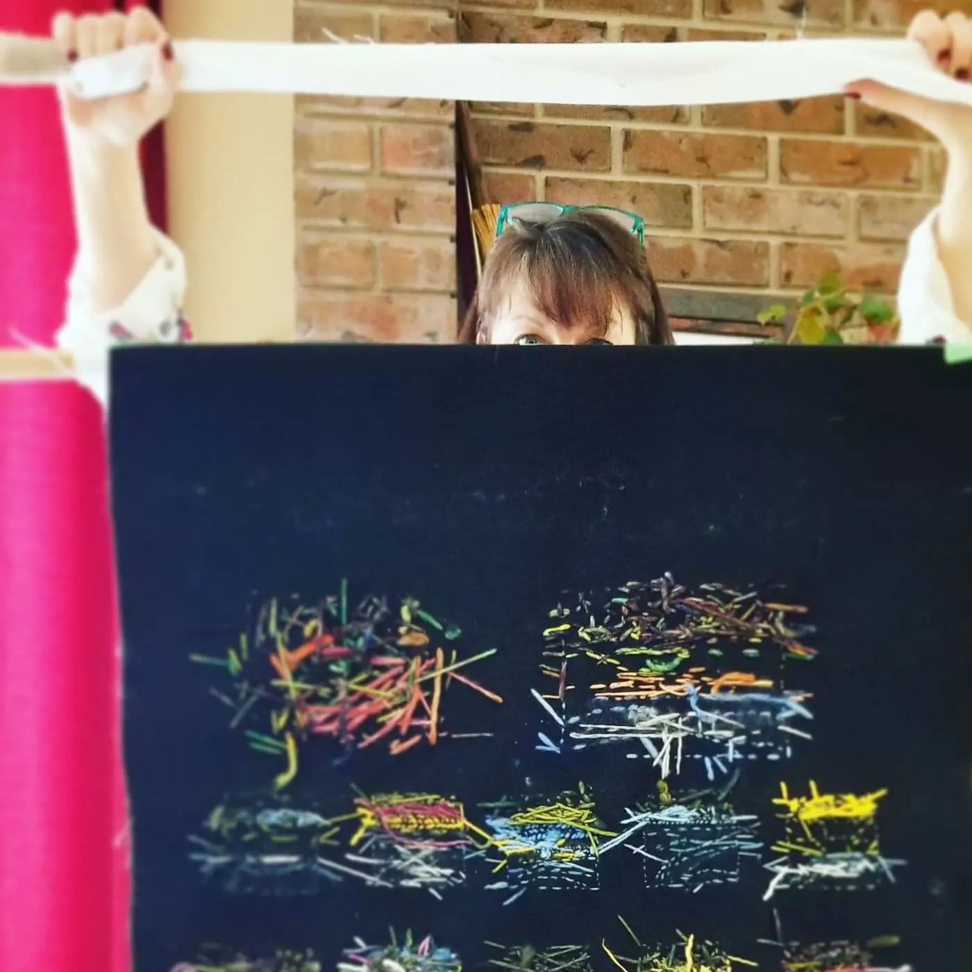Female artist stood behind a piece of abstract stitched artwork, holding the piece up to show the random stitches on the reverse