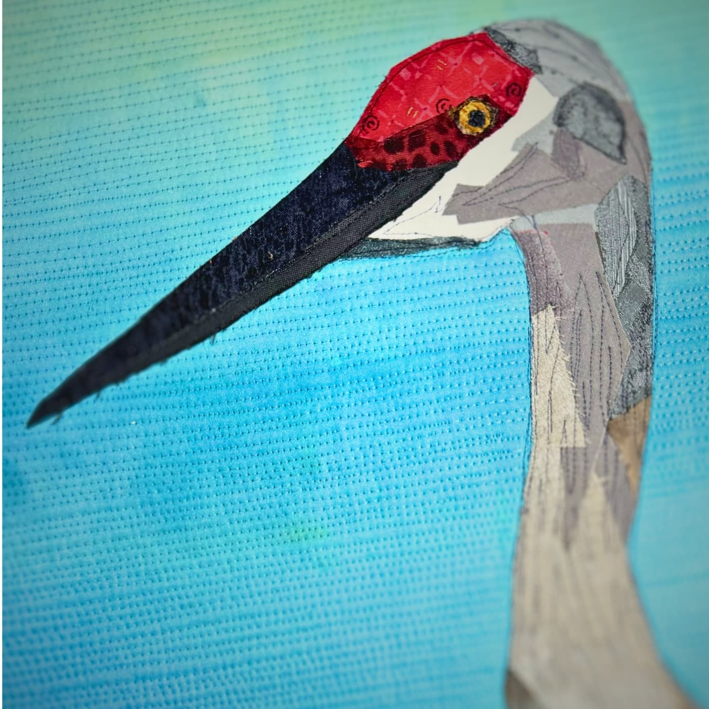 A stitched artwork of a crane bird with a long beak