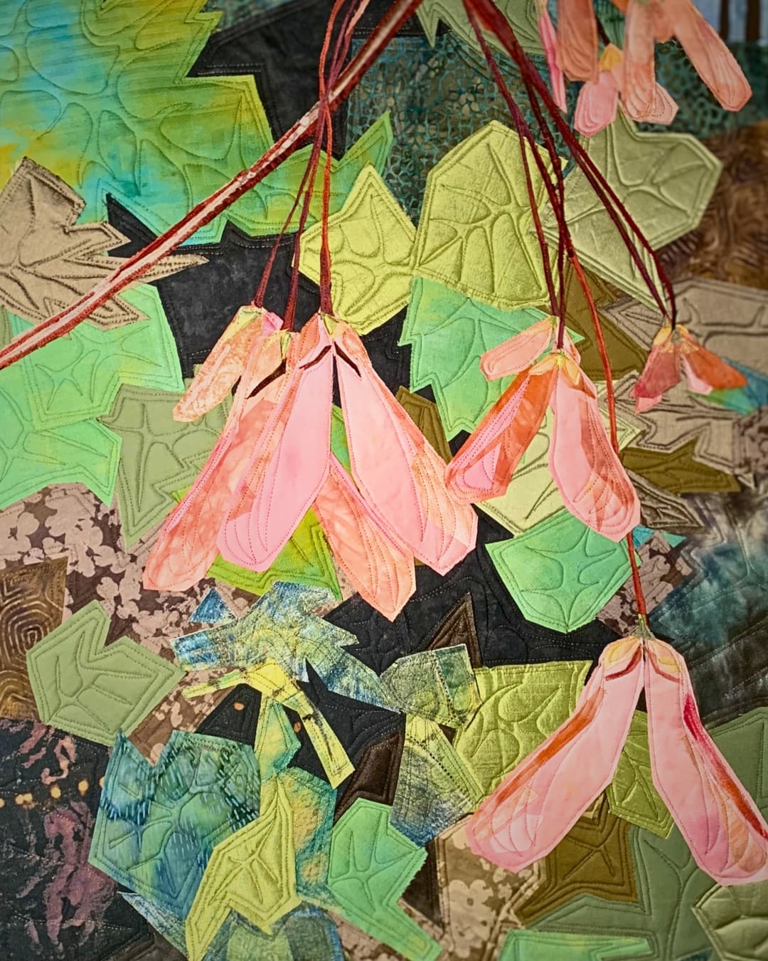 A close up stitched art piece featuring hanging plants and leaves