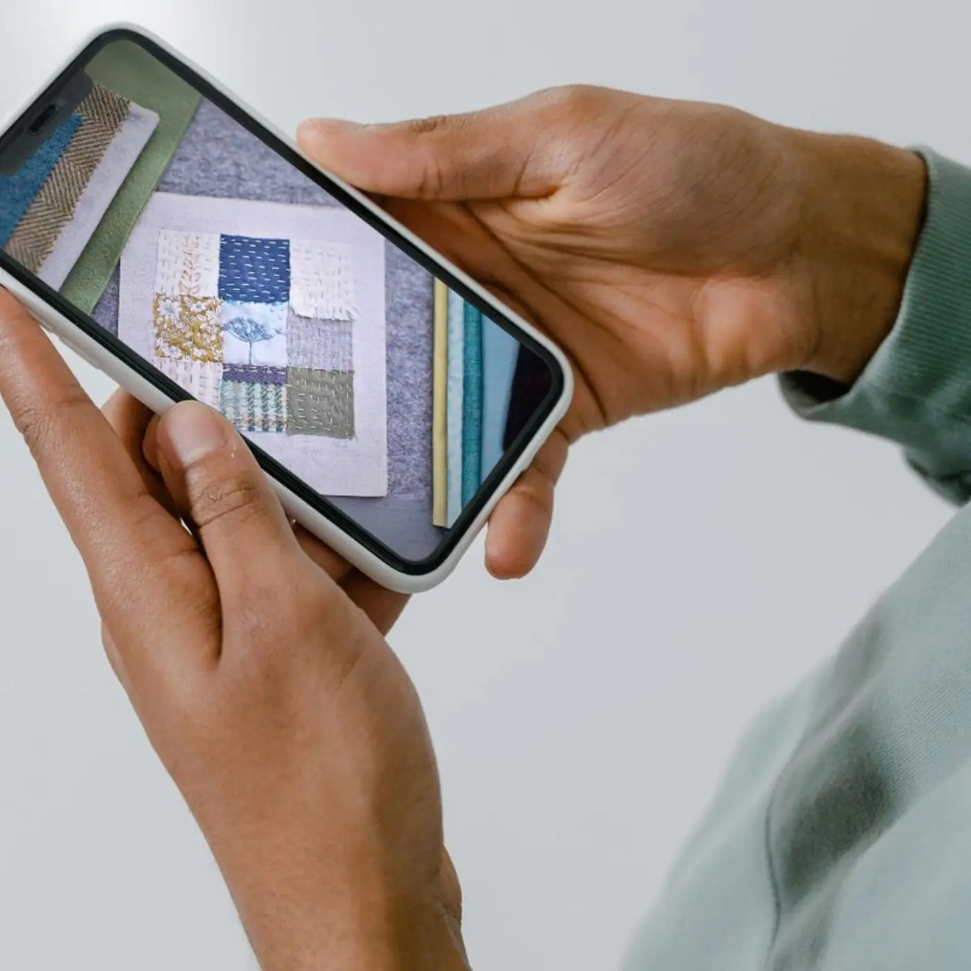 a hand holding a cell phone with a photograph of a textile art sample on the screen.