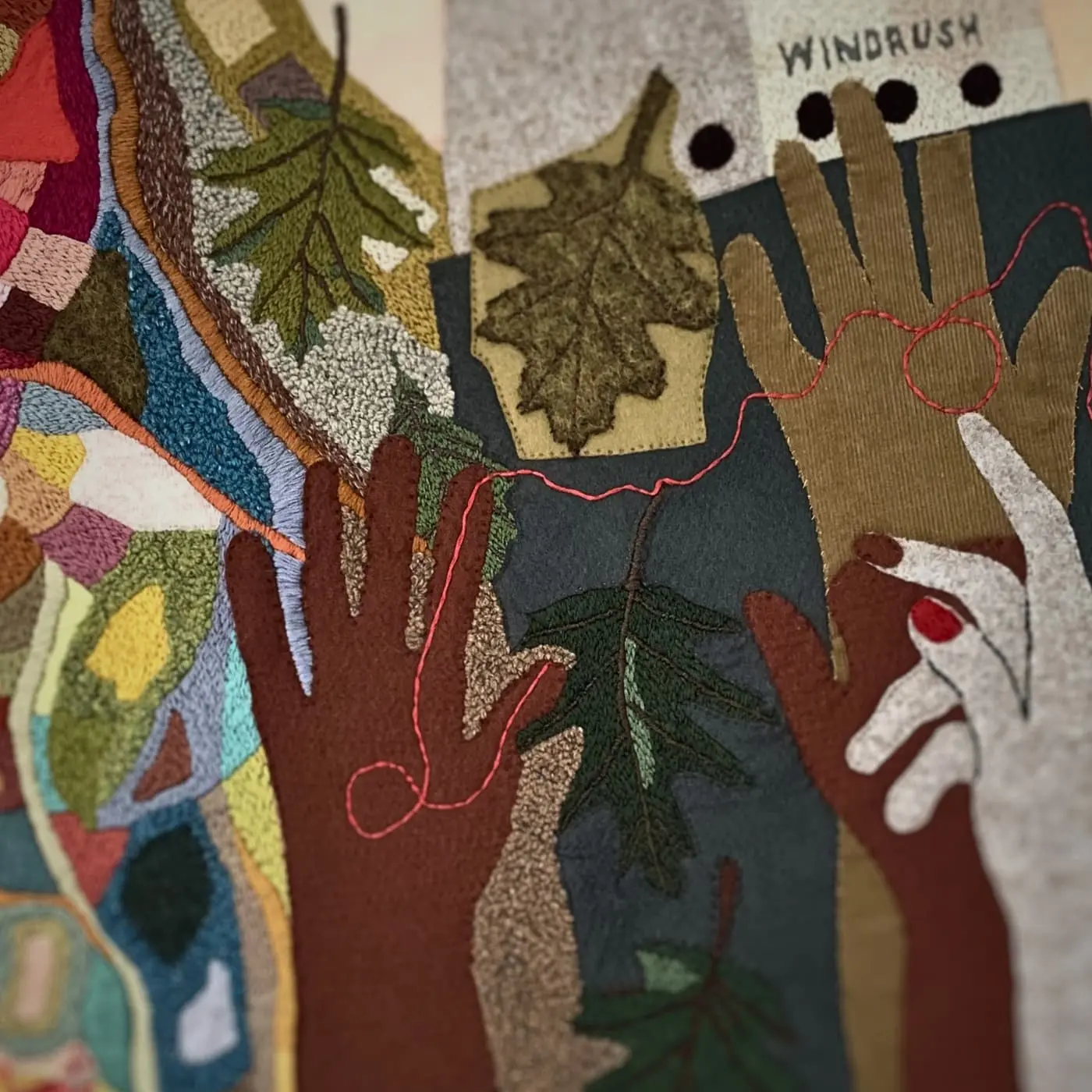 A close up of a fabric artwork depicting stitched hands reaching upwards