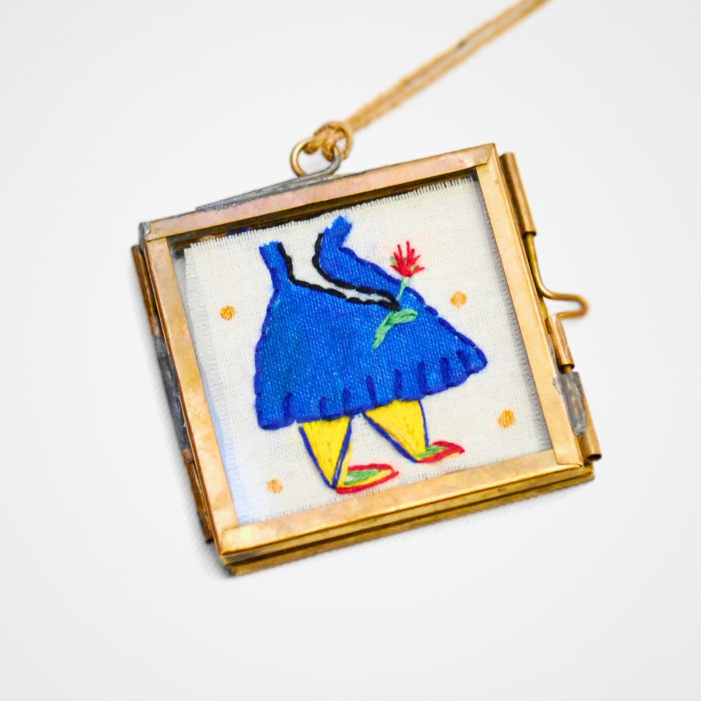 A stitched drawing of a woman holding a flower in small metal frame