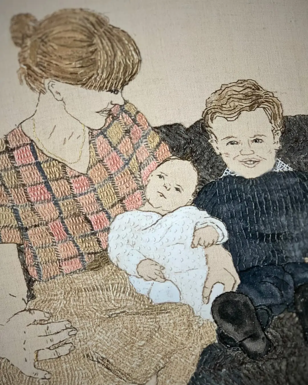 Textile art piece showing mother holding child, seated together.